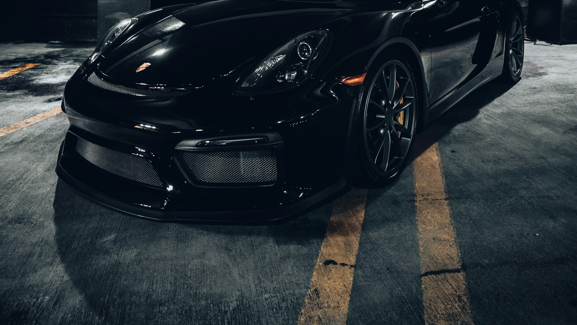 Installer in black gloves smoothing clear paint protection film onto the hood of a dark sports car in a Houston detailing bay